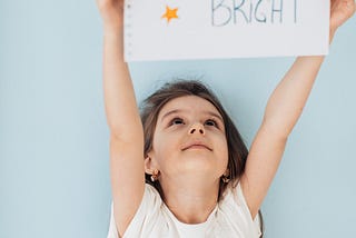 Little girl holding up a sign that says ‘Shine Bright’