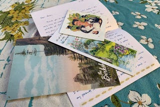 On a white and turquoise tablecloth, my first letter is laid out. It includes a postcard of mountains, a bookmark of green fields and a Frida Kahlo transfer.