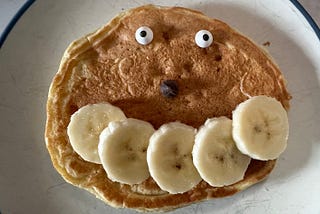 Pancake with googly eyes, a chocolate chip nose, and bananas for a smile