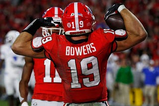 Brock Bowers of the University of Georgia football team flexes his muscles with the football in his right hand.