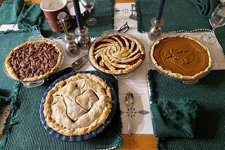 Four pies on a table with green placemats. Two candles and ice cream are behind the pies.