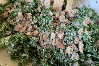 A green kale salad with bits of bread and a spatula sticking out of it.