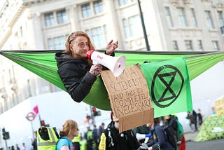 A guy having fun protesting for the environment, with a cardboard saying: “I’m a scientist and this is completely necessary”