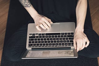 author seated cross-legged typing on laptop