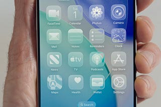 An iPhone screen filled with app icons on the transparent, Liquid Glass user interface.