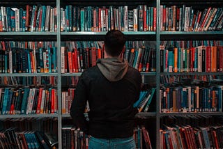 A person looking at an overcrowded bookshelf.