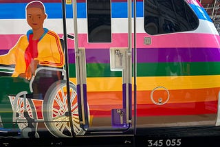 Top of the rainbow train with a old-fashioned video. The wheelchair user is a black teenager with a yellow sports jacket.