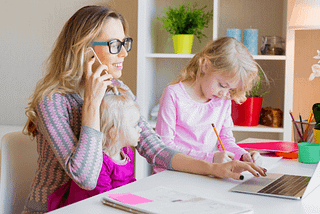 Lady working from home while children entertain themselves at her desk