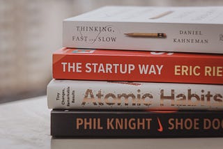 stack of self help books including Atomic Habits and The Start Up Way