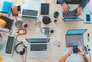 People crowded around a desk using laptops and mobiles