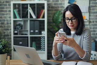 A woman working at a desk with a laptop and a smartphone