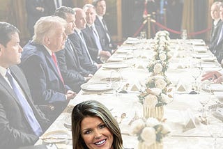 Lindsey Galligan popping up in front of a table full of men and whatever Trump is called these days.