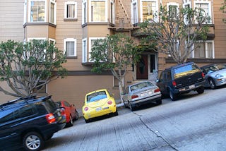 A car rolling downhill, on Nob Hill in San Francisco, past several other cars parked on the slant