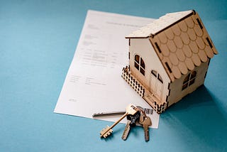 Piece of paper next to a small wooden house and a set of keys.