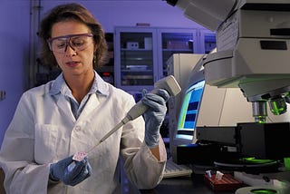 NIST biomedical engineer Laurie Locascio wears safety glasses and a lab coat as she places a water sample on a chip.