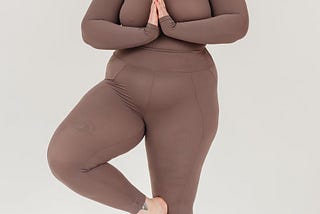 A woman in brown yoga clothing in Tree Pose.