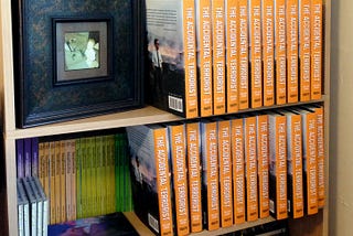 A bookshelf containing various objects, including two dozen hardcover copies of The Accidental Terrorist.