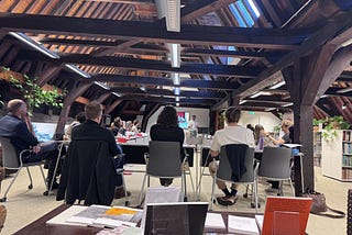 Abhay presenting to academic staff in room with many wooden roof beams above