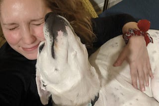 Laura, in a black sweatshirt, cuddling her white and black dog, Ivy.