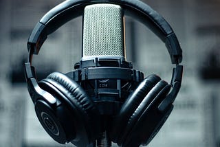 A photograph of headphones hung over a professional looking microphone, like you might expect for a recording studio or podcast