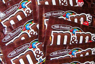 Pile of brown M&M’s milk chocolate bags overlapping each other.