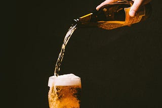 Glass beer bottle pouring beer into an already filled pint glass.