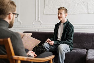 A teenage boy, sitting on a couch, speaking to his therapist