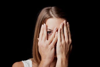 nervous woman covering her face on black background