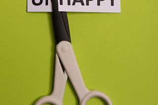 A pair of scissors cutting the word “unhappy”