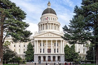 A photo of the state capital building, a stately white building with a tall dome and green trees on both sides.