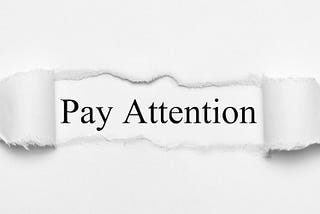Image of words “Pay Attention” revealed behind torn pieces of paper.
