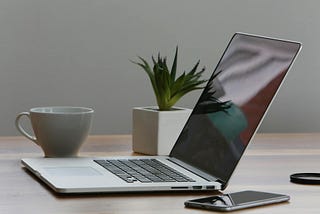 silver laptop and white cup on table — you don’t need an ‘all signing and dancing’ laptop to start your business.