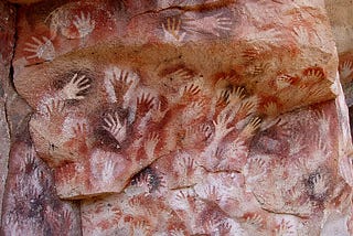 Handprints of a cavemen on a cave, made from spraying something to the cave with hands sticking to the wall, leaving marks.
