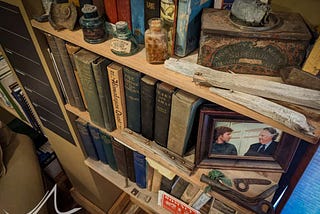 Bookshelf in my office containing the fascinating trash/treasure collected over the years, including a battery from 1922, Everest postcard from 1924, a pill bottle from 1933, piton from 1938, piton hammer from 1960, and more.