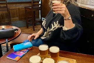 Woman sitting at a pub table with six small glasses of beer