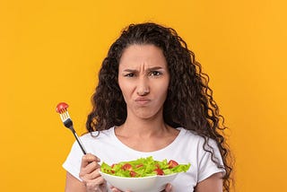 A young woman holding a salad and looking unsure.