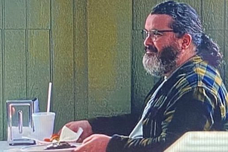 Dave sits at a table in a restaurant in a scene from “The Bear” on FX
