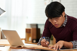 Young engineer wearing glasses and maroon sweater studying at computer