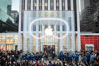 Apple Vision Pro event in NYC Apple store, showing clear glass building with apple logo and shape of the googles behind it.