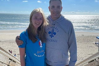 Author stands with his arm around his daughter with the beach and ocean in the background.