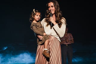 Image of woman talking into a microphone holding a toddler on her hip.