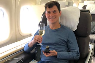 Nomadic Matt sitting in business class on a plane, holding up a glass of champagne