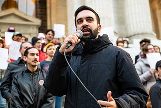 Zohran Mamdani (black coat, front, holding microphone) addresses a crowd at the Resist Fascism rally in Bryant Park on October 27, 2024.