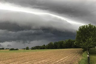 A storm rolls in across an Illinois field. The clouds are looming, gray and ominous, but in the middle there is a streak of lighter sky, like hope.