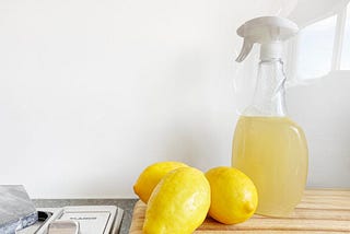 A glass spray bottle filled with a diy cleaning solution made from fresh lemons, vinegar and water, sitting on a wooden surface