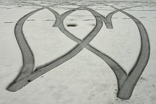 Two hearts in the snow made by tire tracks