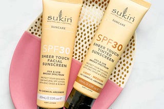 Pale yellow tubes of Sukin Reef Safe Sheer Touch SPF30 Sunscreen in Untinted and Light/Medium on a pink and gold plate