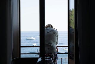 A woman standing on the balcony looks out at the ocean.