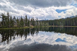 Tree-lined mountain lake with clouds reflected in still water