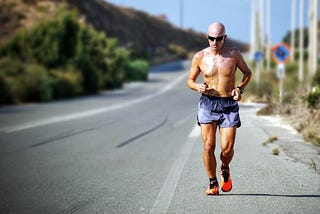 A runner in a pair of shorts running beside a long straight road